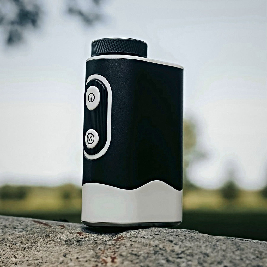 SEASONS rangefinder resting on stone with a golf course in the background