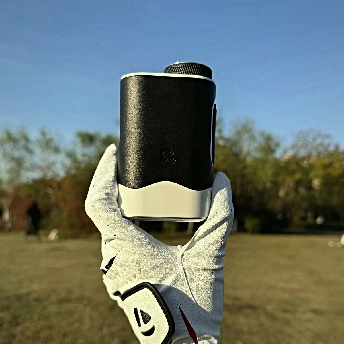 Golfer holding the SEASONS rangefinder in a white glove against a blue sky